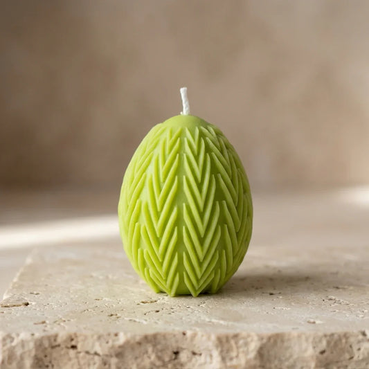 Close-up of a hand-poured green soy wax egg candle highlighting its deeply embossed chevron leaf botanical pattern.