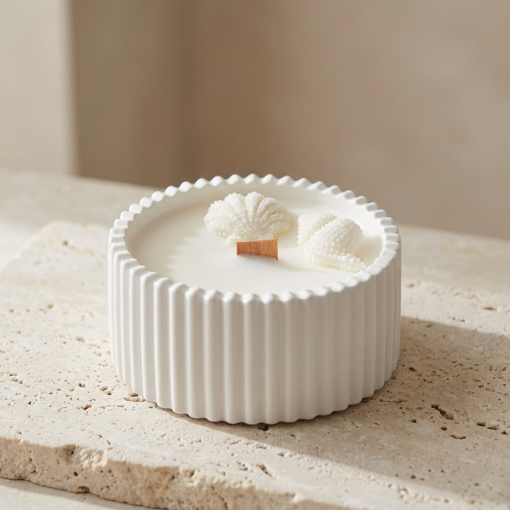 Close-up of a handcrafted ribbed gypsum vessel featuring hyper-realistic wax seashells and a natural wooden wick resting on top of natural white soy wax.