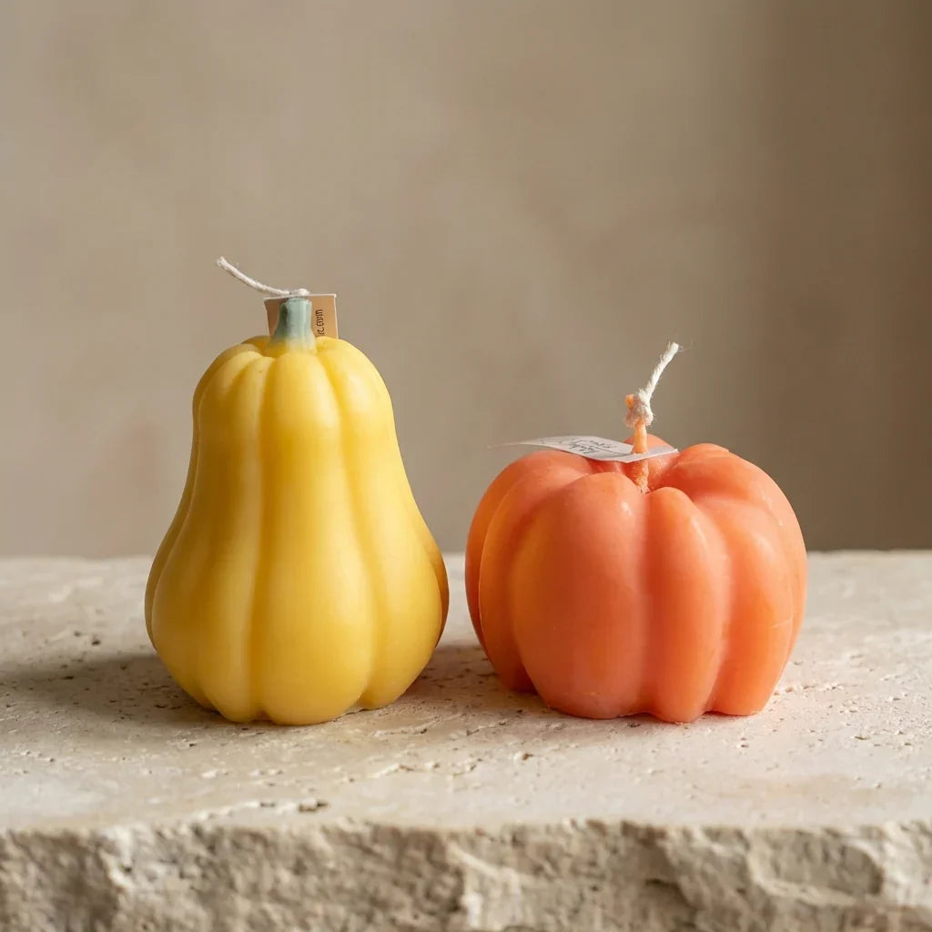 Two decorative candles shaped like a yellow pear and an orange pumpkin on a stone surface.