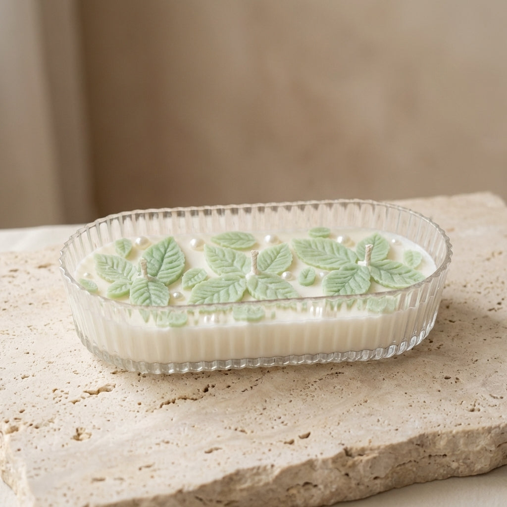 Close-up of a ribbed organic glass oval vessel featuring intricately hand-crafted wax mint leaves and shimmering pearls resting on top of natural white soy wax.