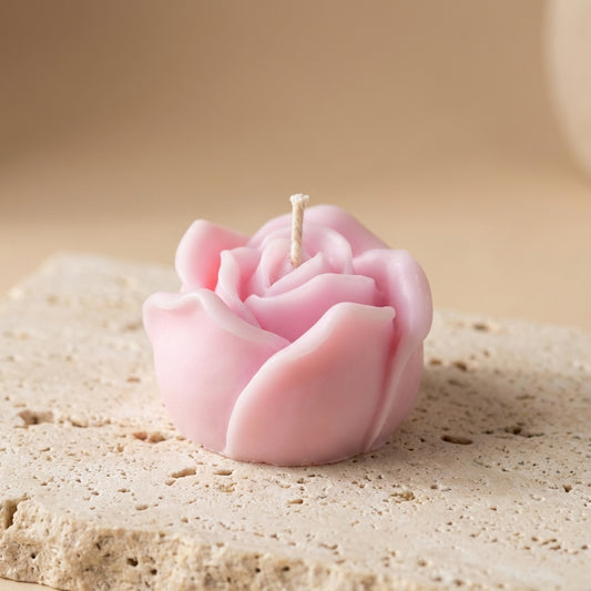 Pink rose-shaped candle on a textured surface with a blurred background