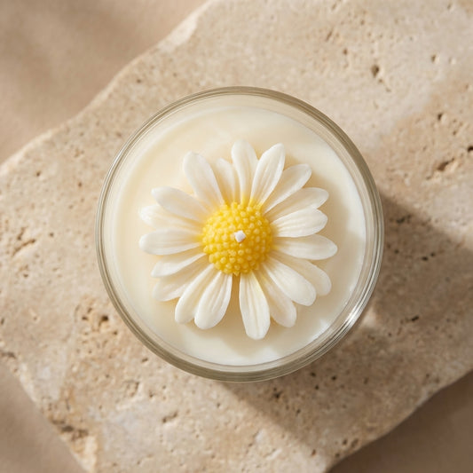 Close-up of a clear glass candle jar featuring a meticulously hand-crafted, two-toned wax daisy resting on top of natural white soy wax.