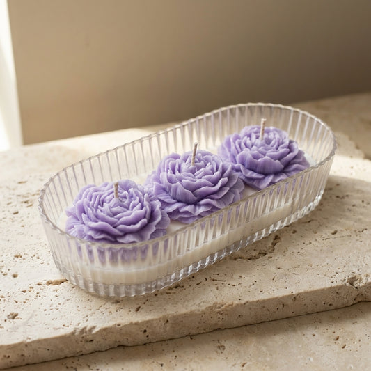 Close-up of a ribbed acrylic oval vessel featuring three intricately detailed pink wax peonies resting on top of natural white soy wax.