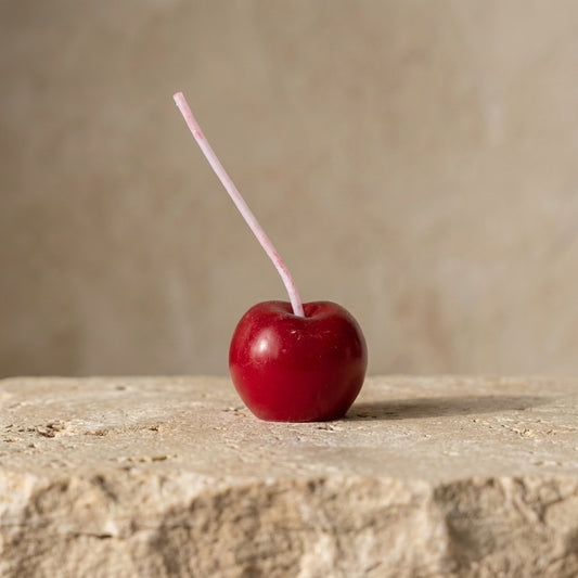 Close-up of a hand-poured soy wax cherry cake candle highlighting its hyper-realistic glossy red finish and extra-long wick stem.