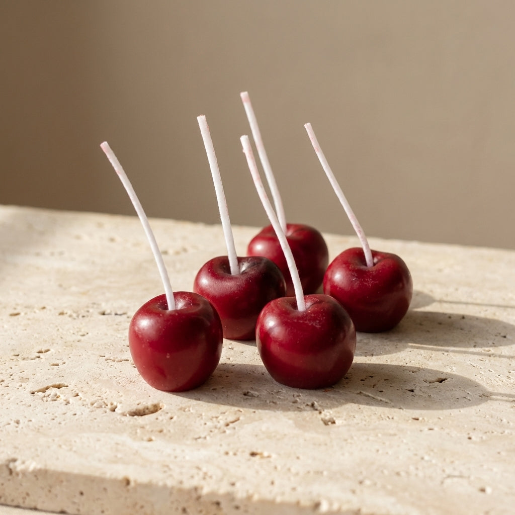 Close-up of a hand-poured soy wax cherry cake candle highlighting its hyper-realistic glossy red finish and extra-long wick stem.