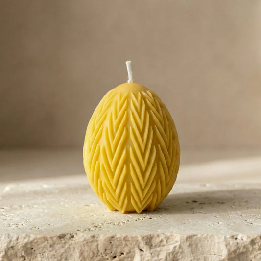 Close-up of a hand-poured yellow soy wax egg candle highlighting its deeply embossed chevron leaf botanical pattern.