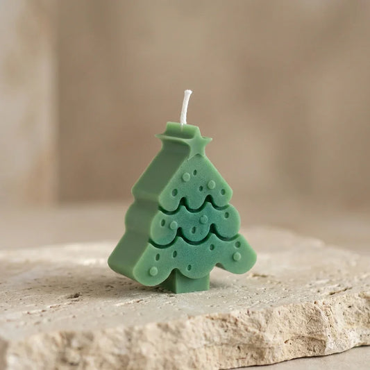 Green Christmas tree-shaped candle on a stone surface with a blurred background