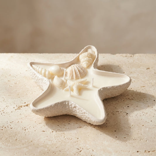 Close-up of a handcrafted starfish-shaped gypsum vessel featuring three wicks, intricate wax seashells, and a miniature wax starfish on top of natural soy wax.