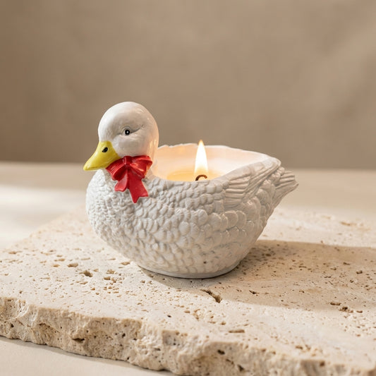 Close-up of a handcrafted gypsum duck vessel featuring a hand-painted yellow beak and red ribbon bow, with natural soy wax poured into a hidden heart-shaped cavity.