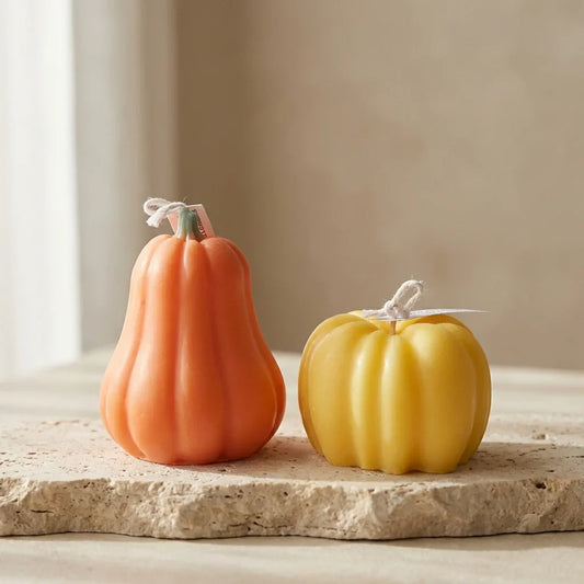 Two decorative pumpkins, one orange and one yellow, on a stone surface with a neutral background.