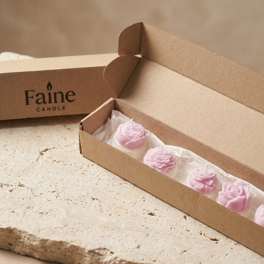 Open box of Faine Candle with pink rose-shaped candles on a stone surface