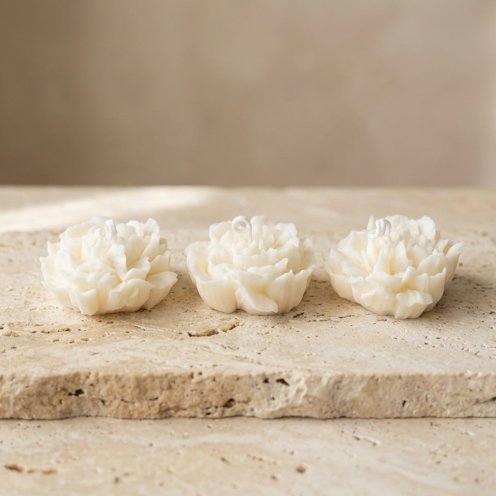 Three white flower-shaped candles on a beige stone surface