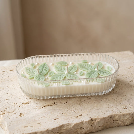 Close-up of a ribbed organic glass oval vessel featuring intricately hand-crafted wax mint leaves and shimmering pearls resting on top of natural white soy wax.