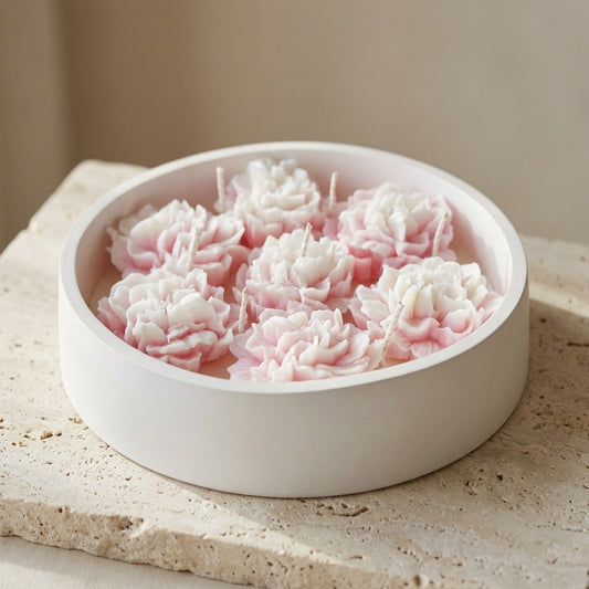 Close-up of a large, handcrafted matte gypsum bowl featuring seven wicks and a lush arrangement of intricately detailed pink and white wax peonies resting on top of natural soy wax.