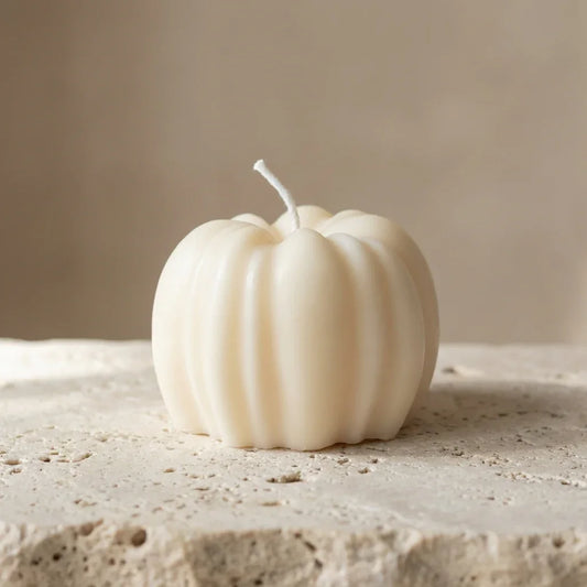 White pumpkin-shaped candle on a textured surface with a neutral background