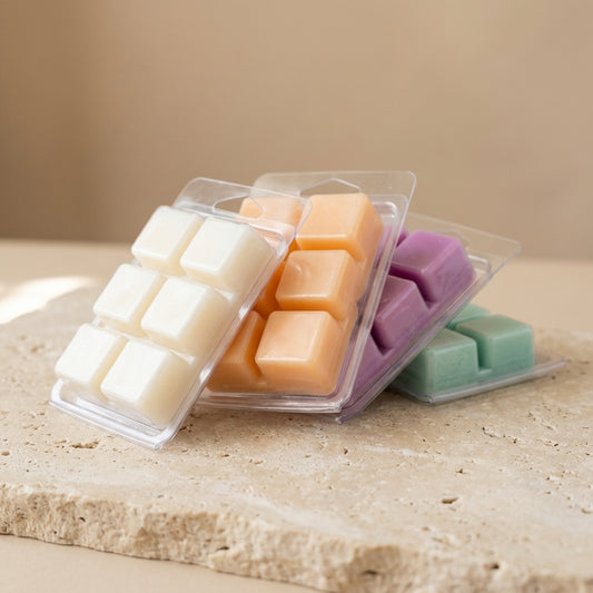 Three clear containers with square wax melts on a stone surface.