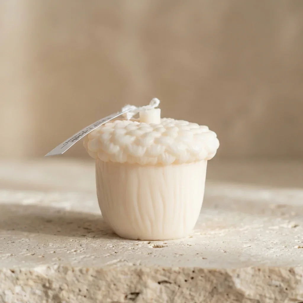 Small white cupcake-shaped candle with a string on a beige surface