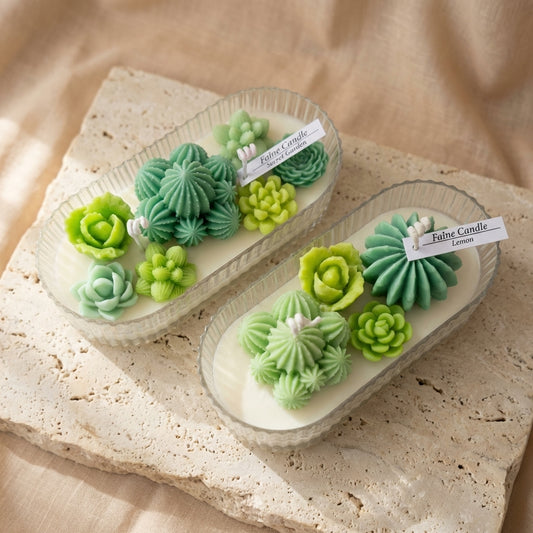 Close-up of a two-wick natural soy candle featuring a lush arrangement of detailed green wax succulents and cacti resting on top.