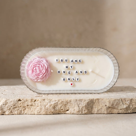 A natural soy candle centerpiece in a clear ribbed vessel revealing the hidden message "YOU ARE MY ONE AND ONLY" in the melted wax.
