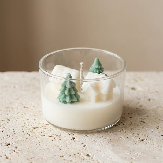 Snowy Forest Village Candle styled on a wooden mantelpiece next to pine cones, creating a cozy and aesthetic holiday atmosphere.