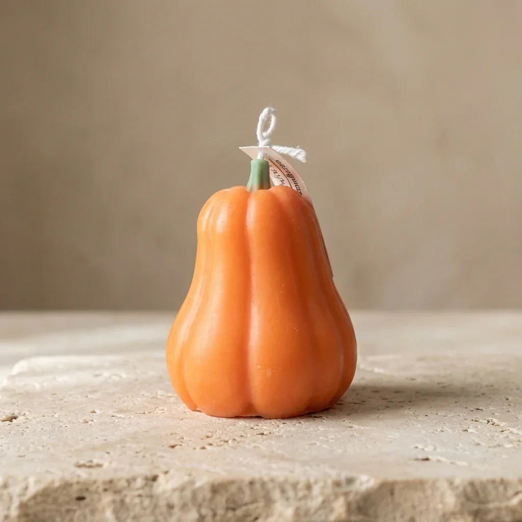 Orange candle shaped like a pumpkin with a green stem on a beige surface.