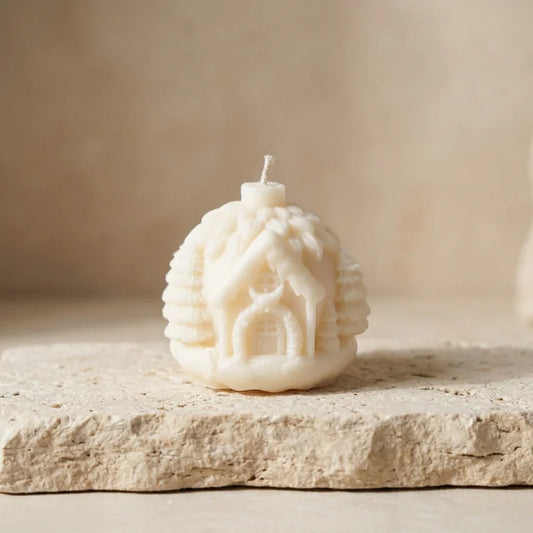 Candle shaped like a small house on a stone surface with a neutral background