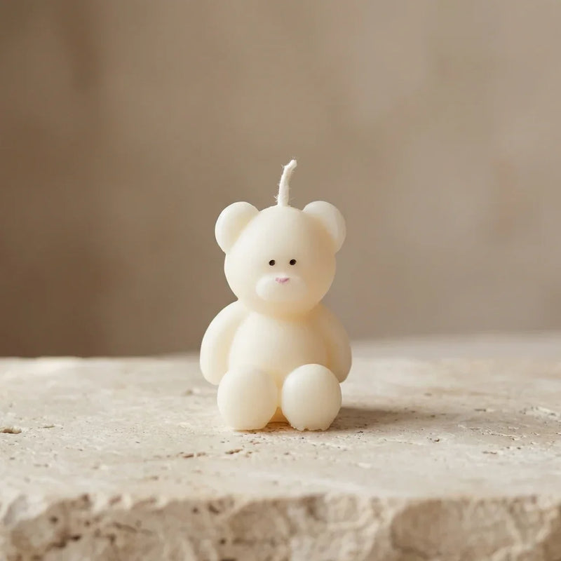 Close-up of a sculptural miniature teddy bear candle made of unscented soy wax, featuring delicately hand-painted eyes and a small pink nose.